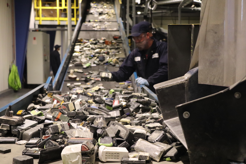 worker bends over conveyor belt full of used electronics