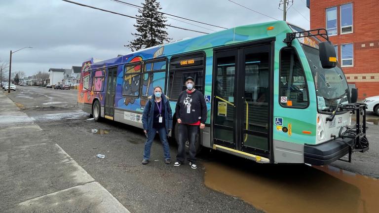 two masked people standing in front of a colourful bus from the article This bus is keeping Thunder Bay’s unhoused out of the cold