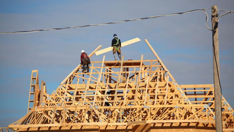 two construction workers on the partially built roof of a house