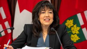 Woman sitting at table and microphone.  from the article What’s ON: The week that was in Ontario politics (November 29-December 3)