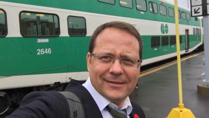 man in suit standing in front of a GO train from the article Could Ontario help lower gas prices by cutting transit fares in half?