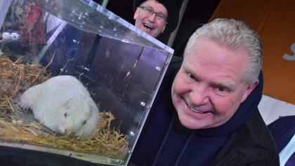 smiling man beside small white animal in a glass container from the article The groundhogs have spoken. Should we believe what they say?